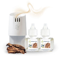 White Scent Fill plug-in diffuser releasing a soft golden fragrance mist beside two Mahogany & Teak refill bottles, with a piece of textured wood on a light background.